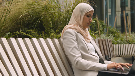 Muslim-Businesswoman-Sitting-Outdoors-In-City-Gardens-Working-On-Laptop-3
